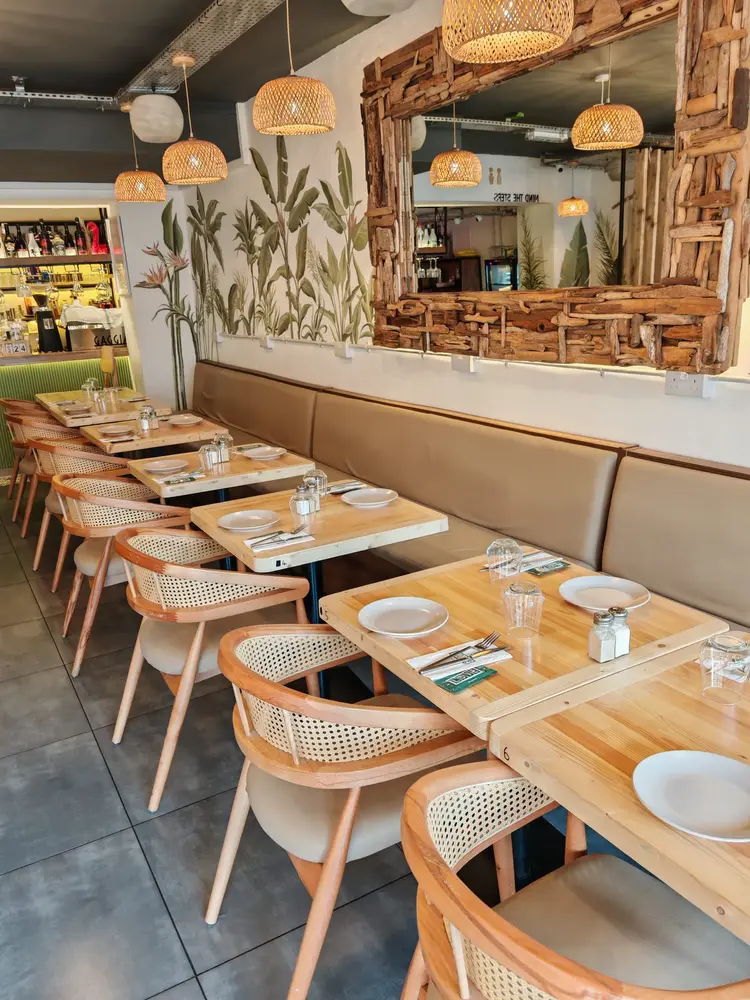 Wooden tables and cane chairs along a tan banquette under woven rattan pendant lights